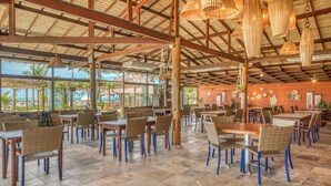 An indoor dining area with wooden tables and chairs, a high ceiling with exposed beams, and hanging light fixtures. - Salinas Maceió All Inclusive Resort (Maceió)