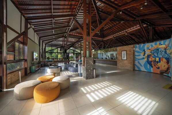 Un hall amplio con techo alto, ventanas grandes y un mural colorido.