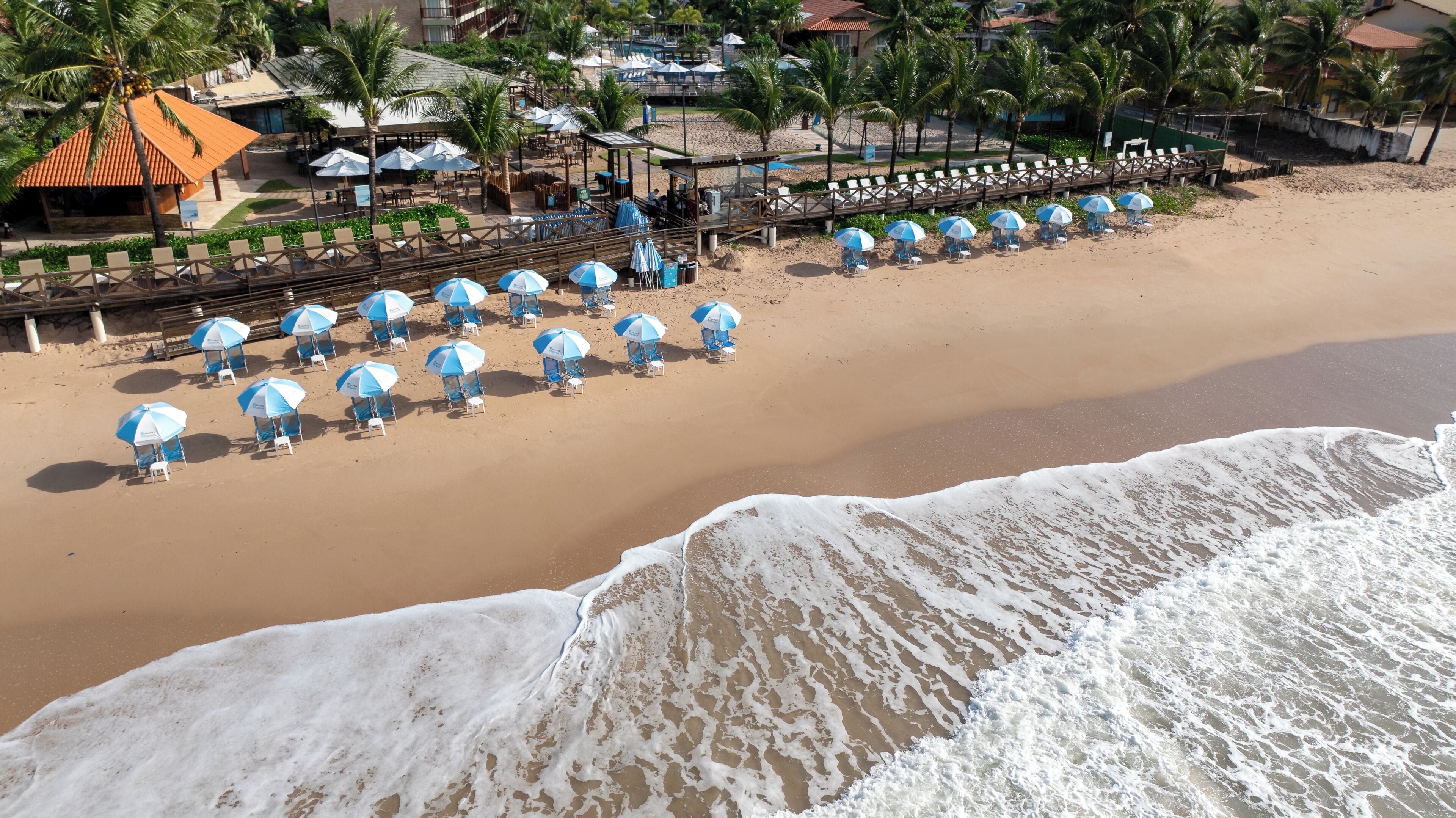 Une plage bordée de rangées de parasols et de chaises longues, une promenade en bois et un bâtiment avec un toit rouge.