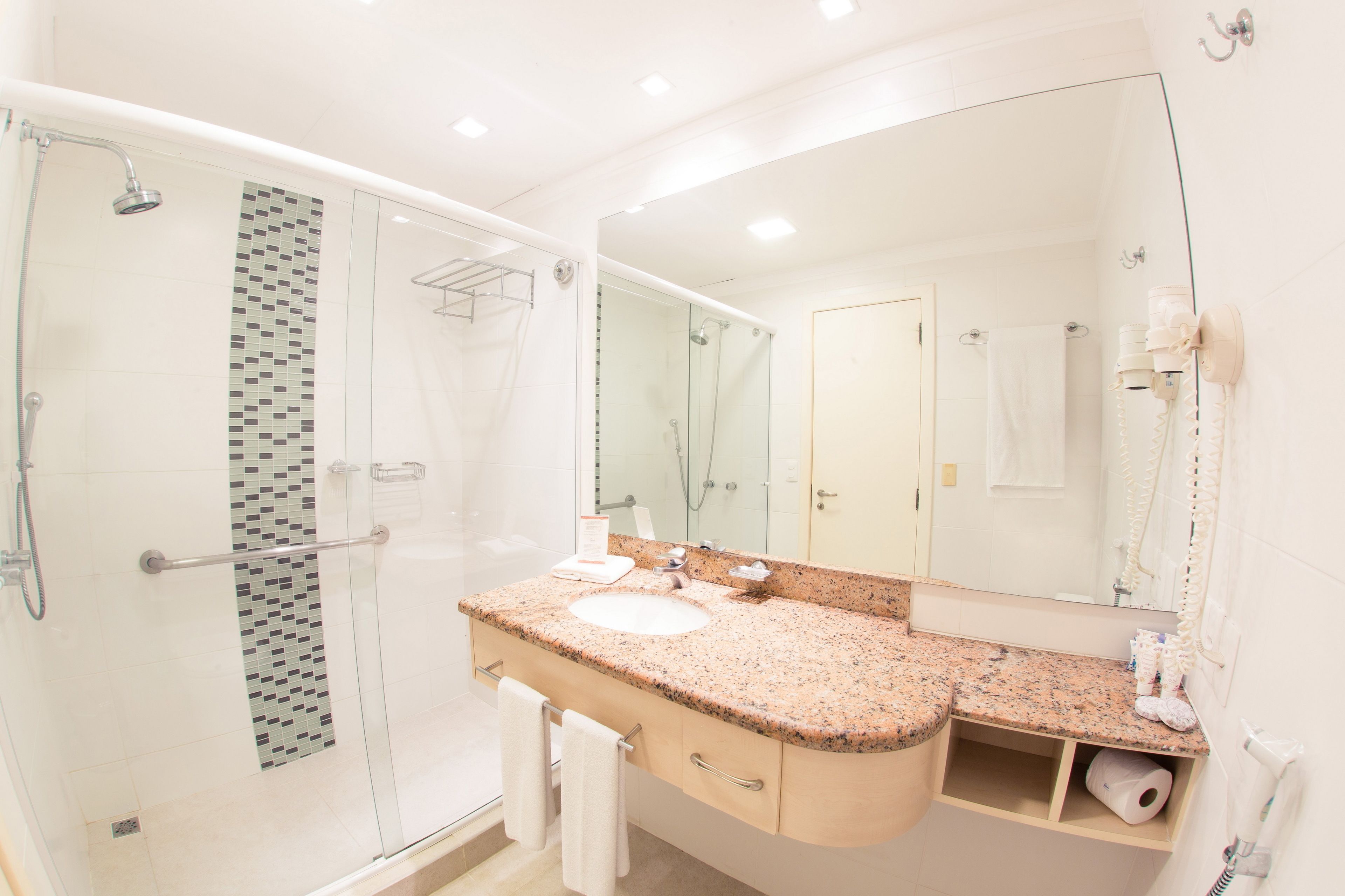 A modern bathroom with a glass shower enclosure, a granite countertop sink, and a large mirror.