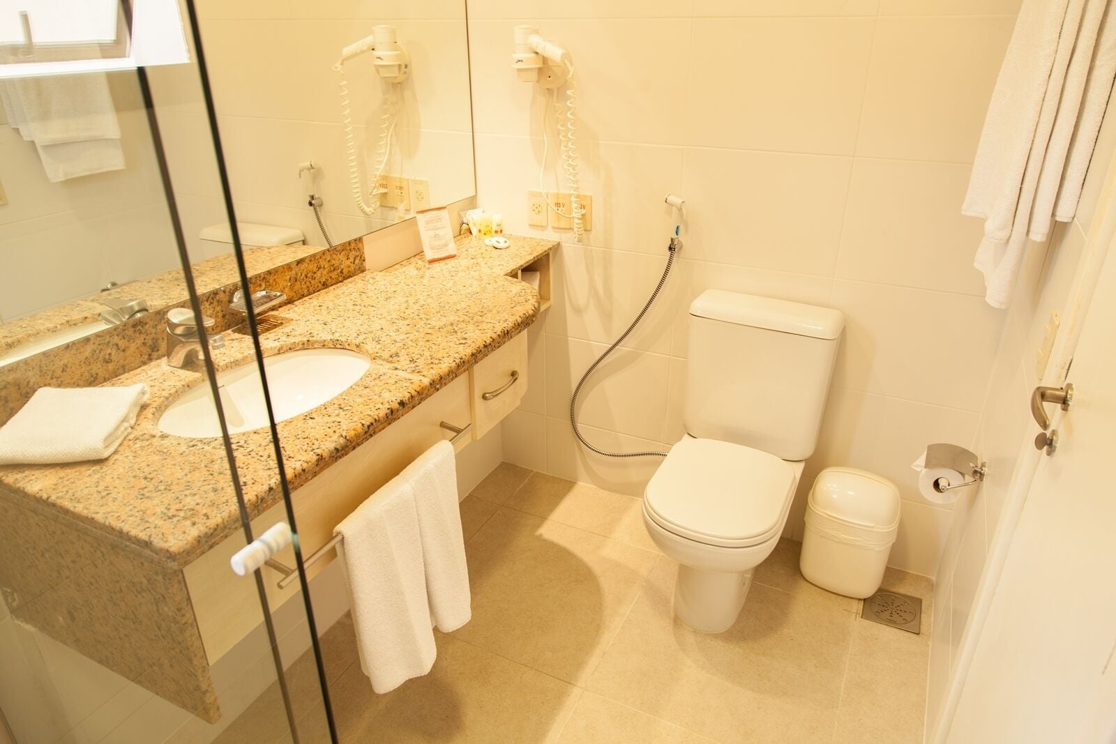 A bathroom with a granite countertop, two sinks, a toilet, and a shower.