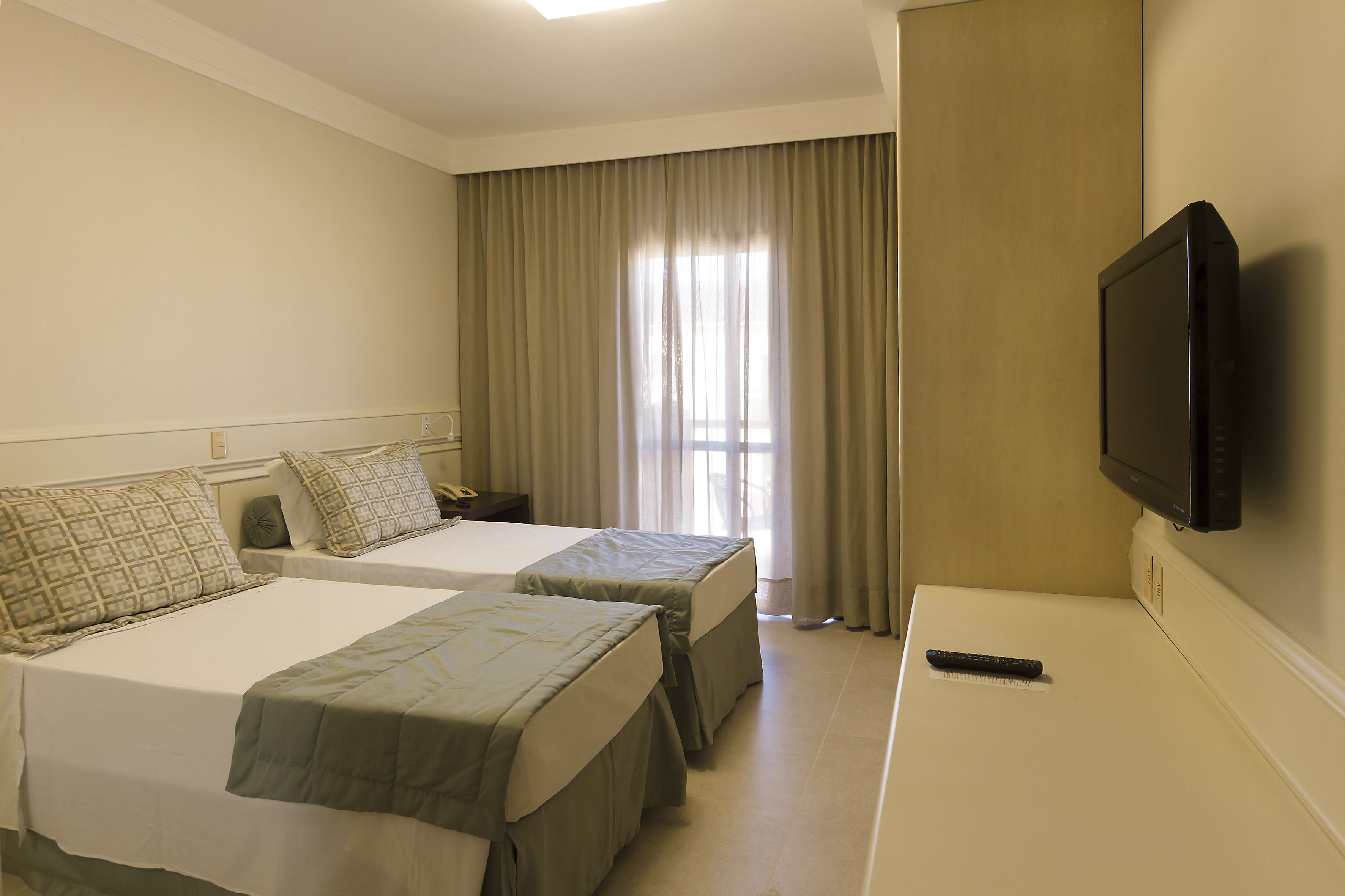 Quarto de hotel com duas camas, televisão e janela com cortinas.