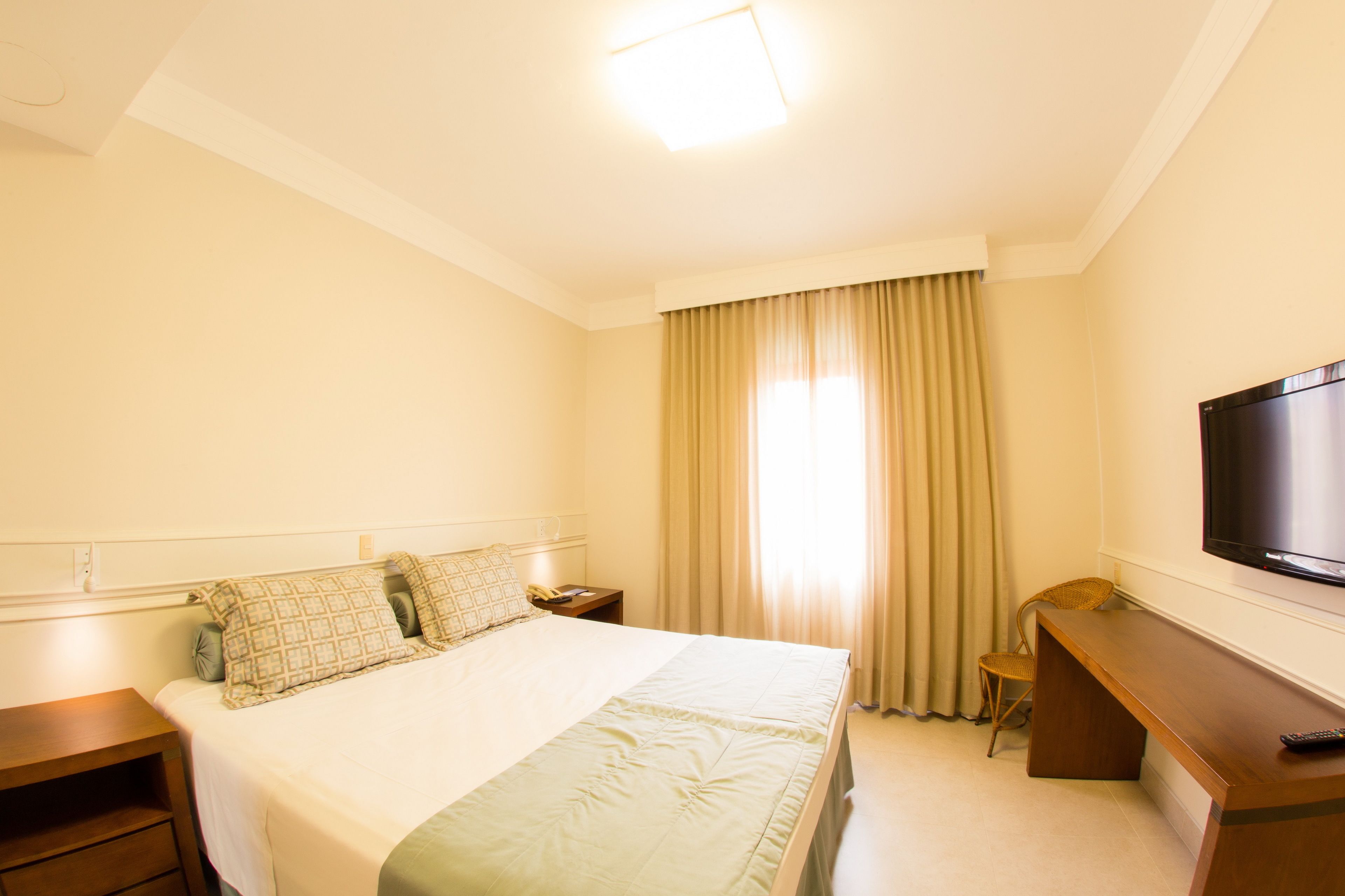 A hotel room with a bed, a desk, a chair, a television, and a window with curtains.