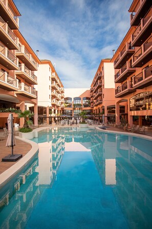 A hotel with a central swimming pool, multiple balconies, and outdoor seating areas. - Hotel Jurerê Beach Village - OFICIAL (Florianópolis)