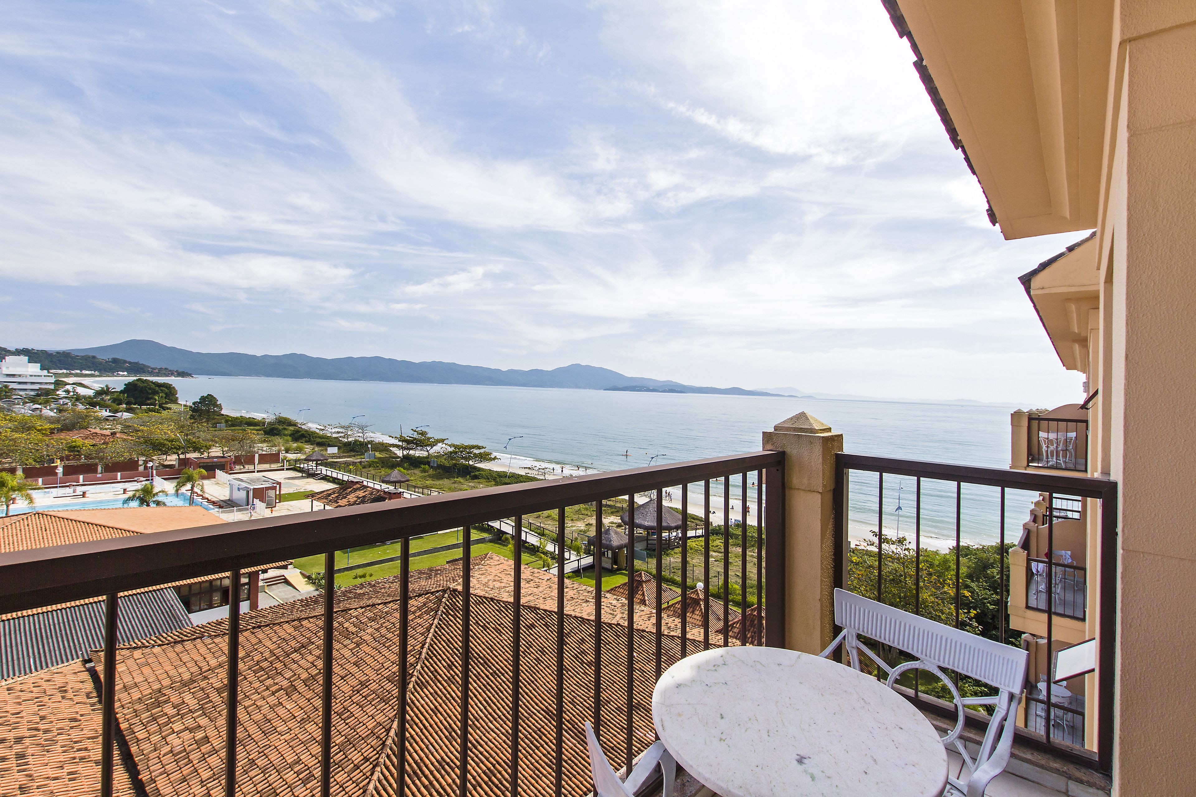 Un balcón con vistas al mar y a las montañas, sillas blancas y un tejado de baldosas.