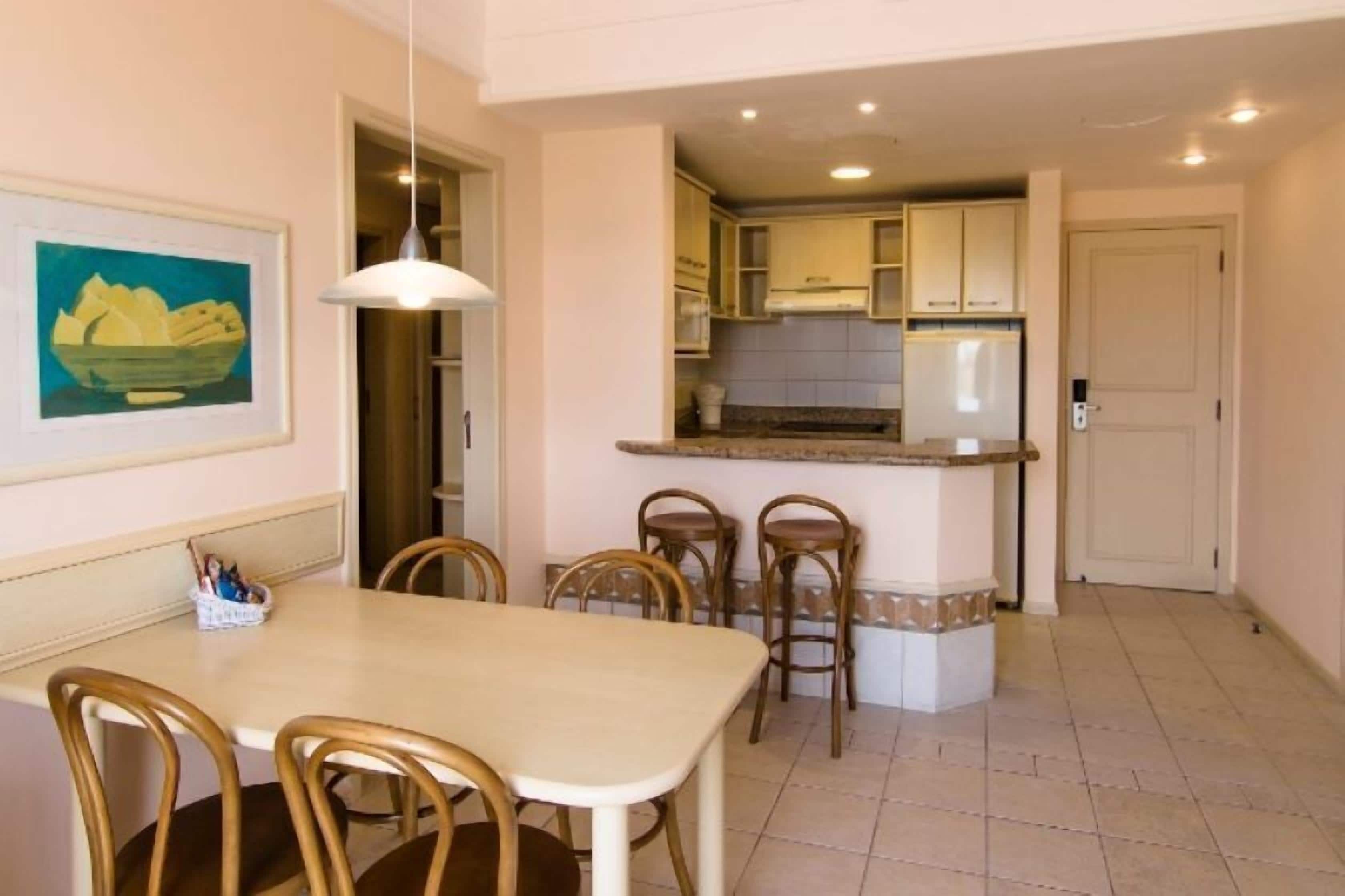Un comedor con mesa y sillas, una cocina con armarios y un refrigerador, y una puerta que da a otra habitación.