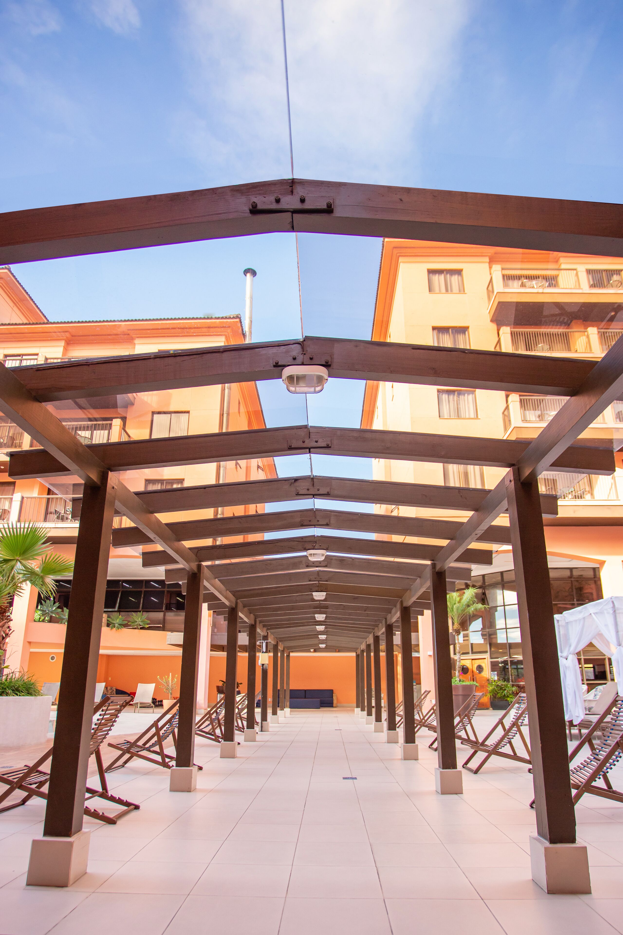 A covered outdoor area with a row of wooden chairs and a clear view of the sky.