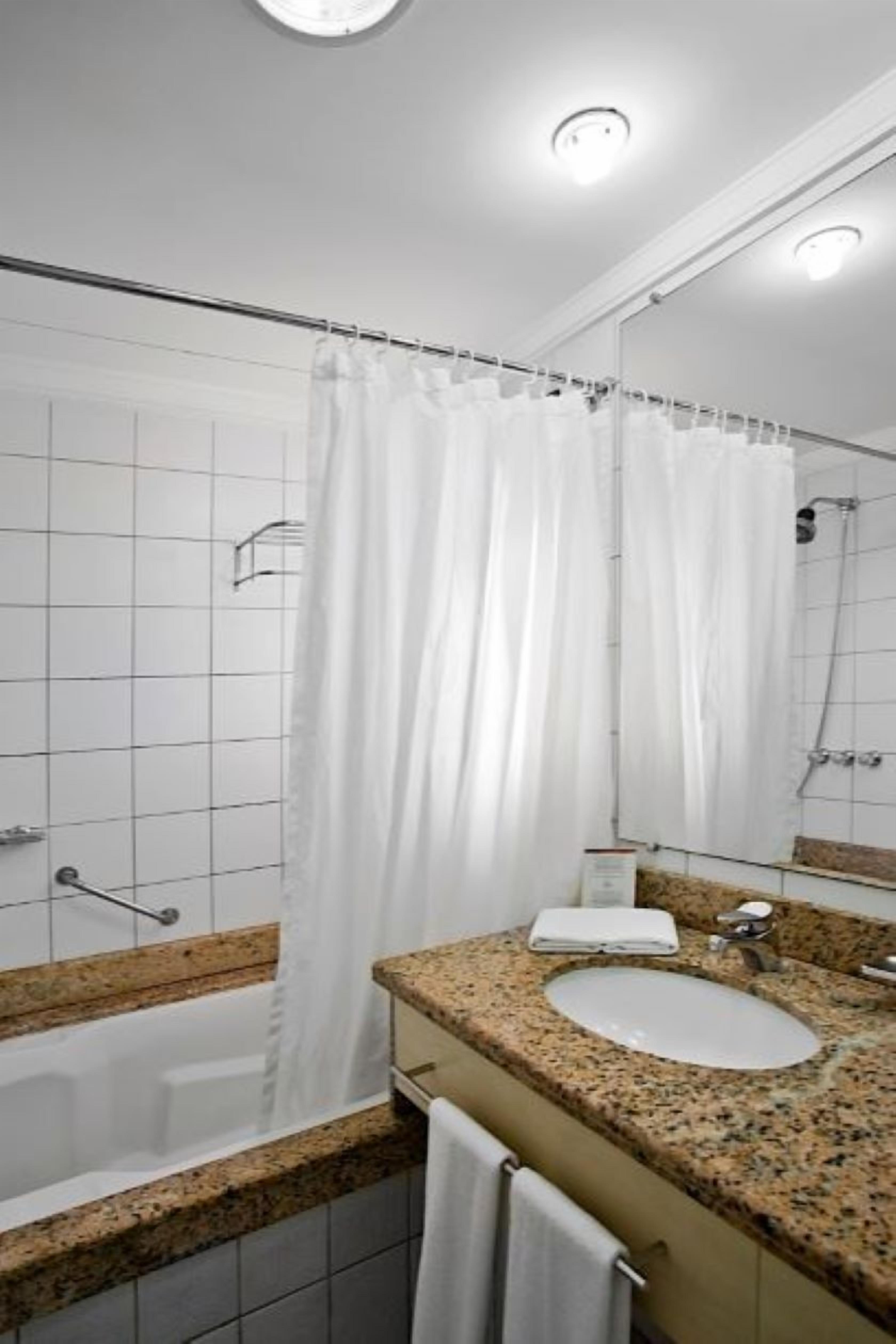 A bathroom with a white shower curtain, a sink with a mirror, and a towel rack.