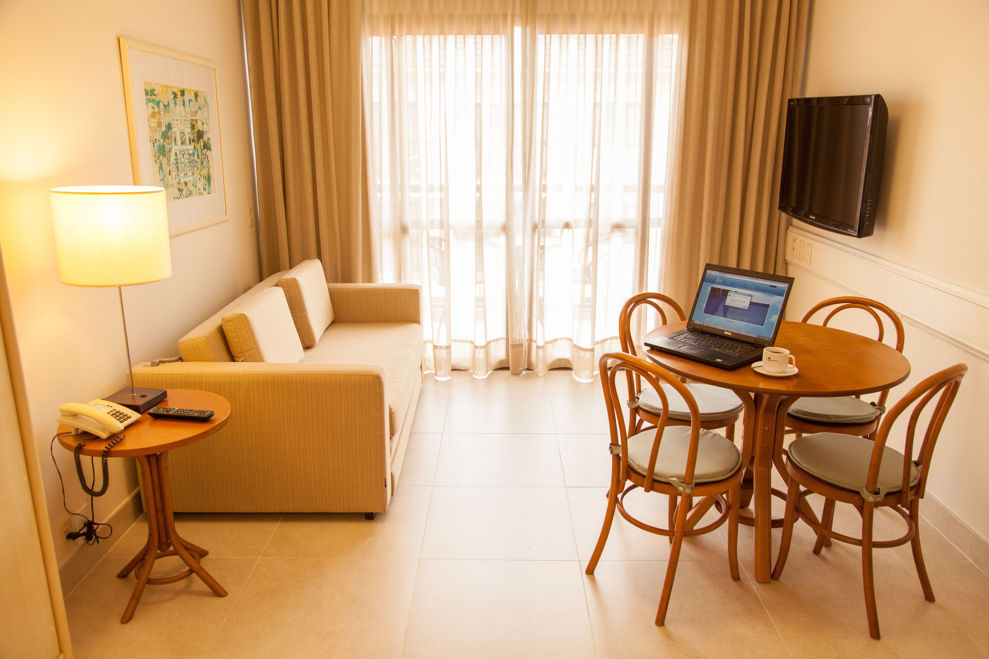 Habitación de hotel con sofá, una mesita con una computadora portátil, televisor montado en la pared y una lámpara.