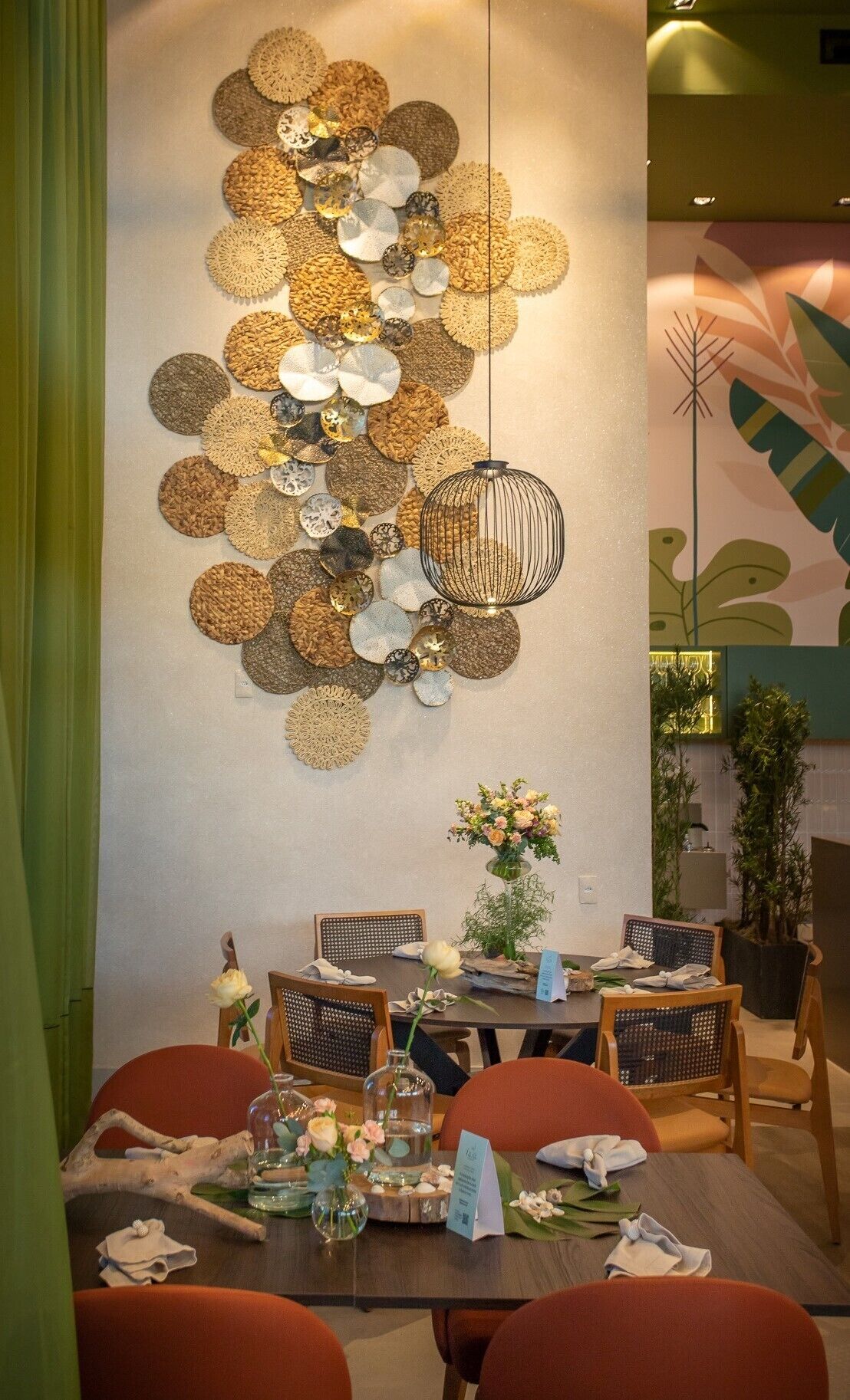 Zona pranzo con un elemento decorativo a parete, una lampada a sospensione e un tavolo apparecchiato per quattro persone con sedie.