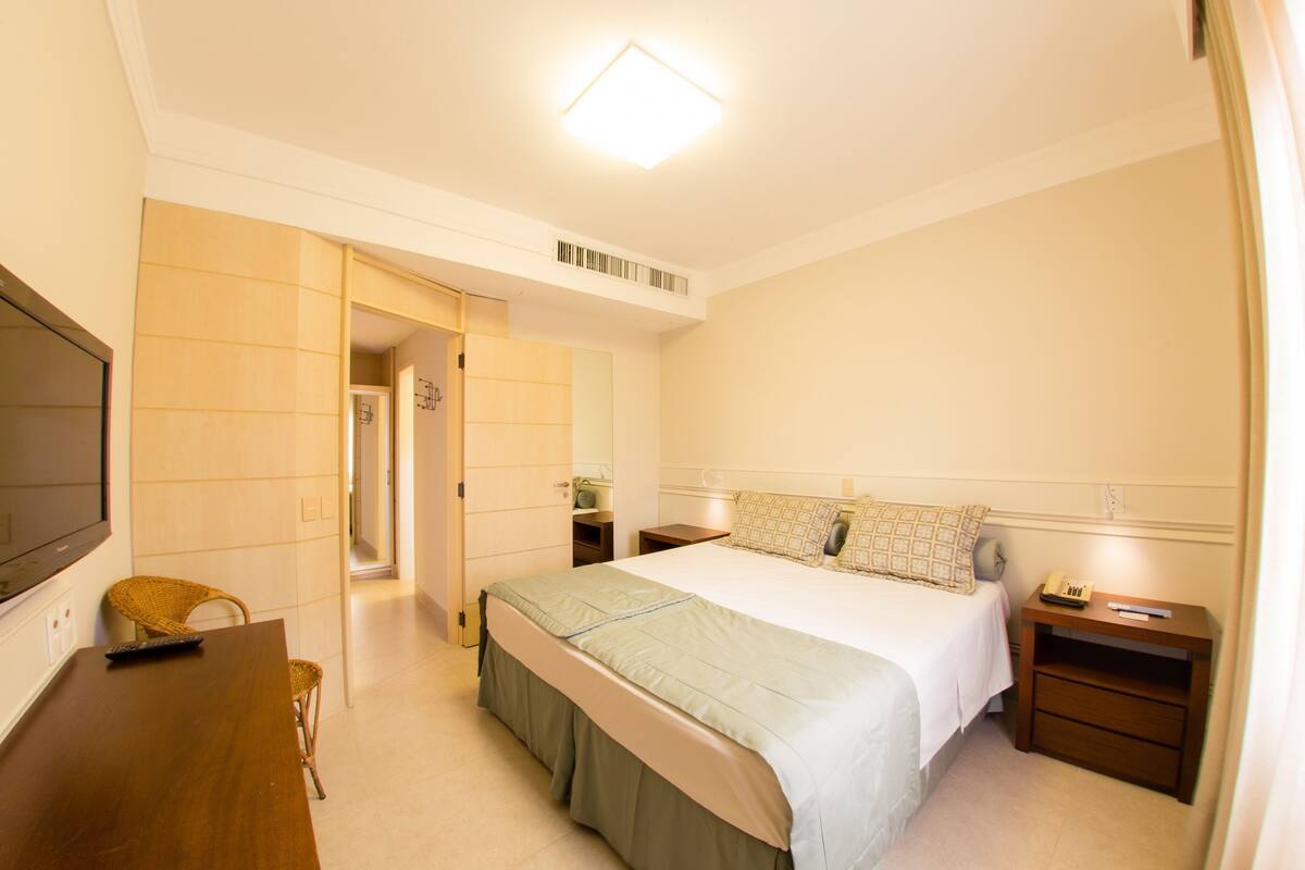 Ein Hotelzimmer mit Bett, Nachttischen, Fernseher und Stuhl.