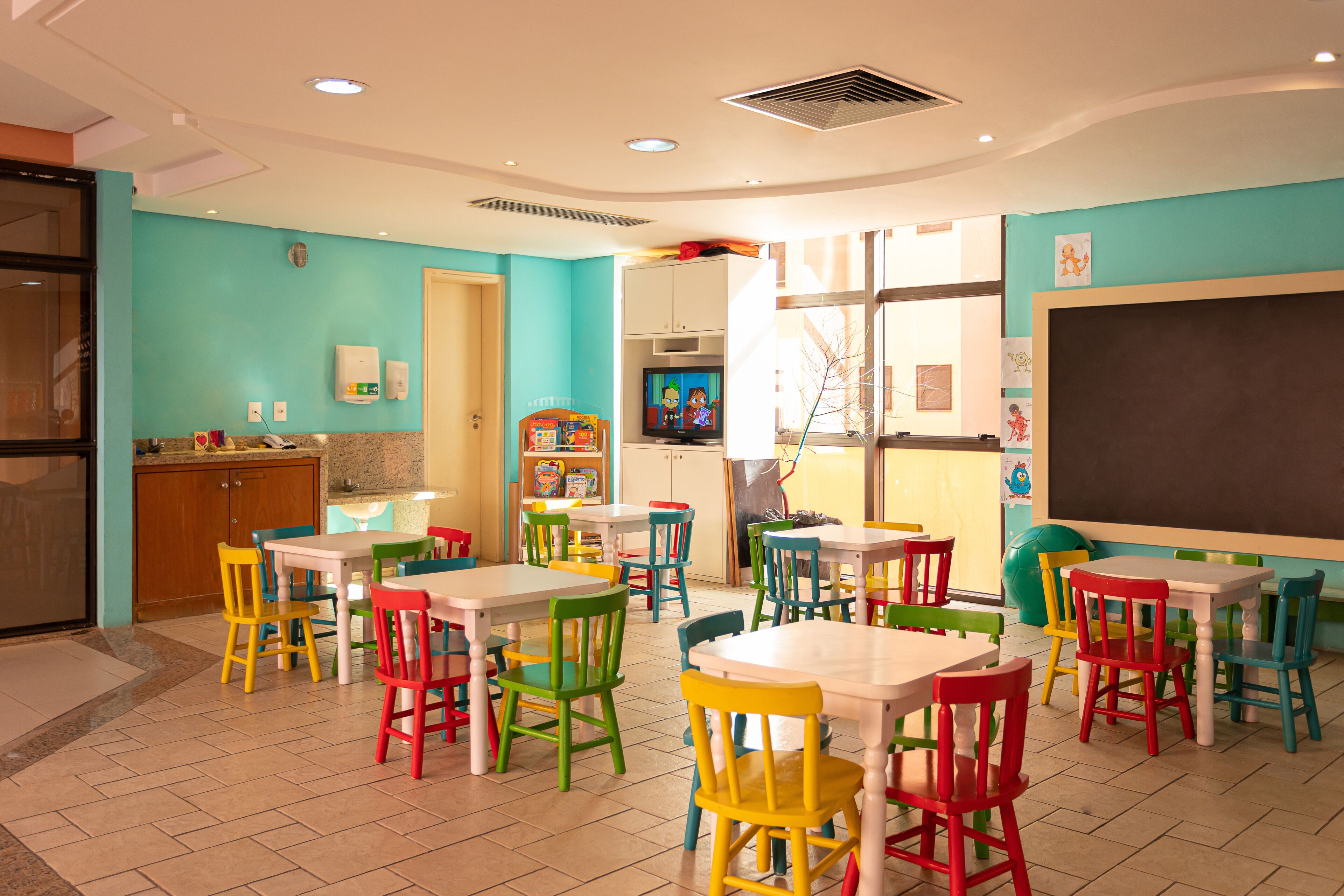 A children's playroom with colorful tables and chairs, a chalkboard, and educational toys.