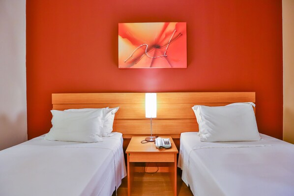 Habitación de hotel con dos camas, cabecero de madera, mesita de noche con lámpara y una obra de arte colgada en la pared.