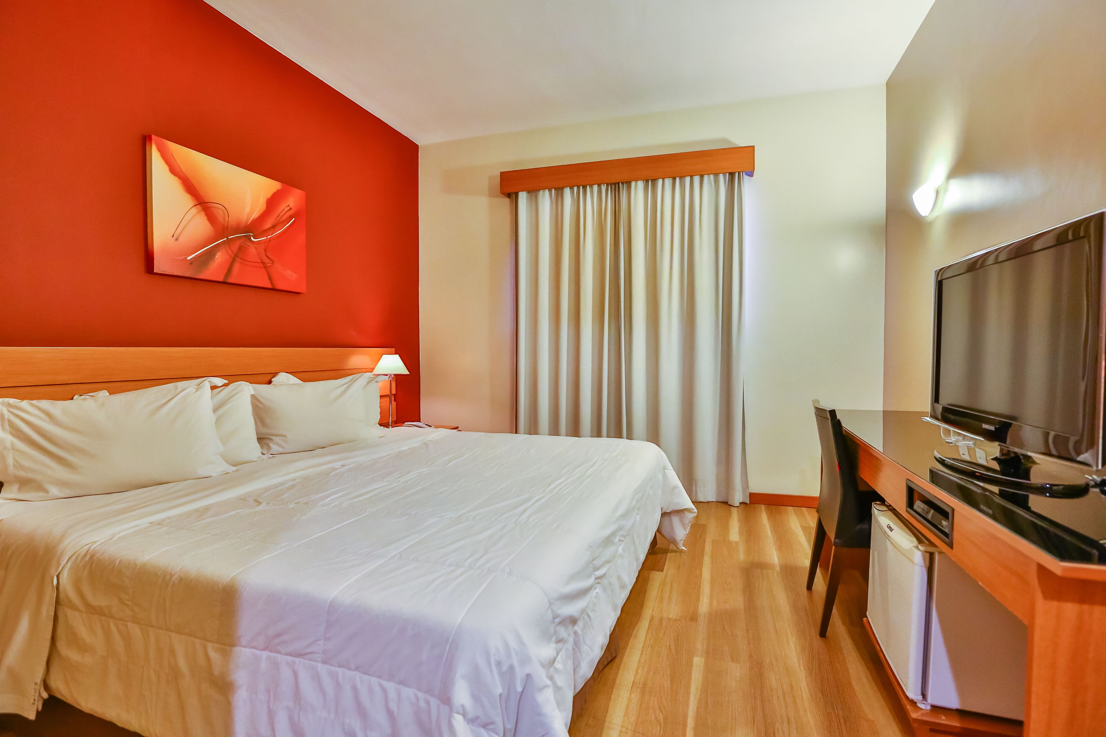 Una habitación de hotel con una cama grande, un escritorio con televisor y una ventana con cortinas.