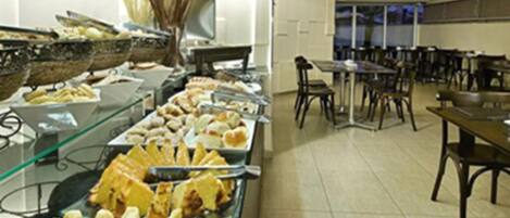 Montaje de bufé con diversos alimentos y una zona de comedor con mesas y sillas.