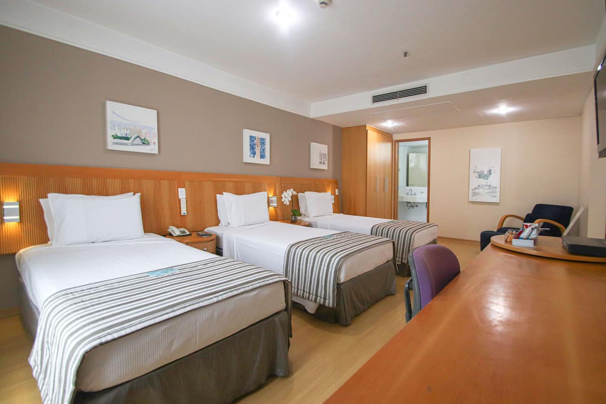 A hotel room with three beds, a wooden desk, and a chair.