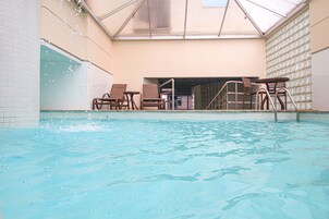 Una piscina interior con agua cristalina, rodeada de paredes de azulejos y un techo de cristal.