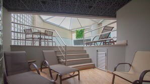 A spacious indoor area with a wooden floor, multiple seating arrangements, a staircase, and a skylight.