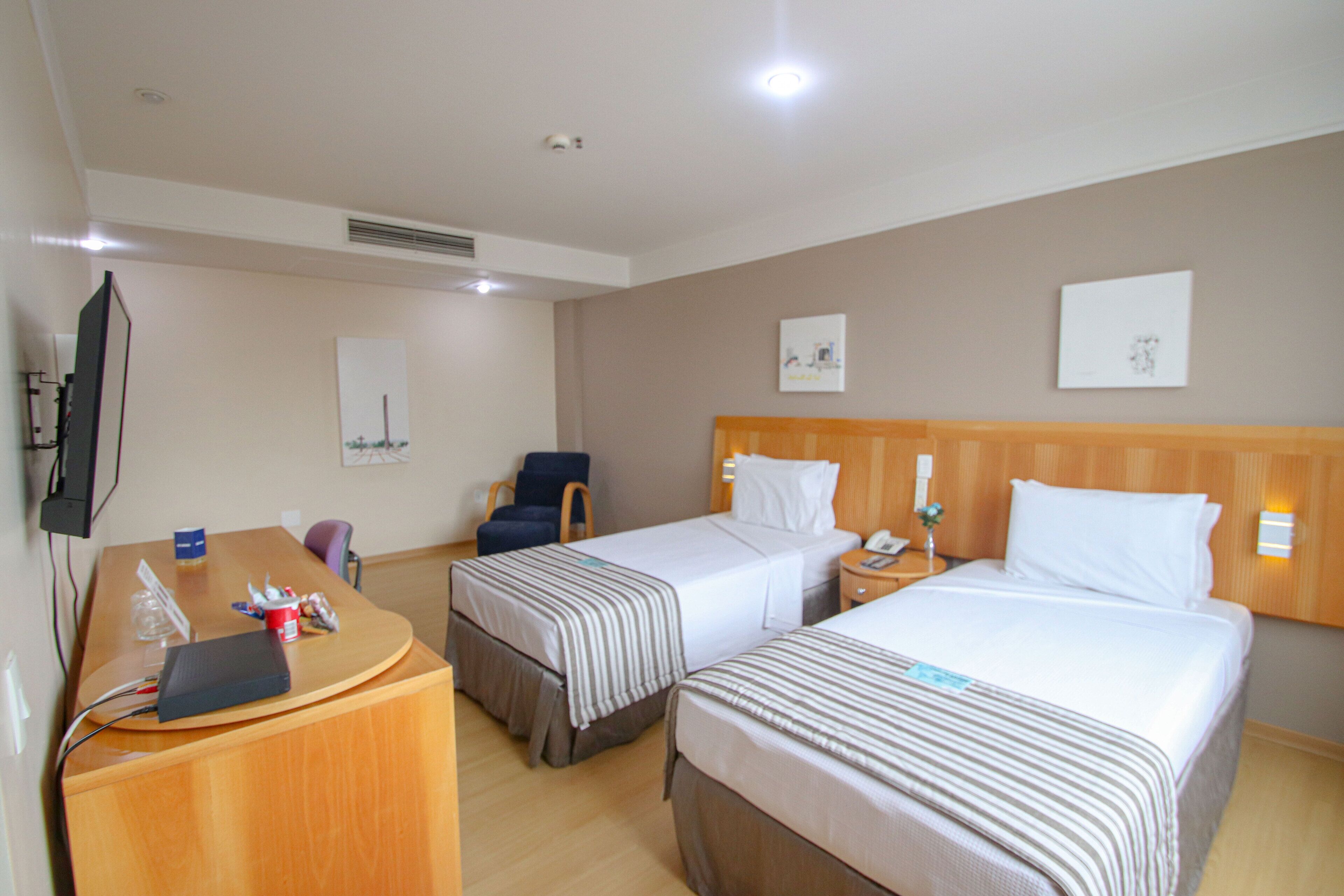 Une chambre d’hôtel avec deux lits, un bureau avec un ordinateur portable, une chaise et un téléviseur.