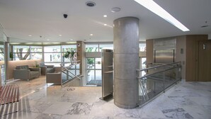 A modern lobby with marble flooring, a central column, and a staircase with glass railings.