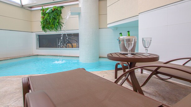 A pool area with lounge chairs, a table with bottles and glasses, and a plant hanging from the ceiling.