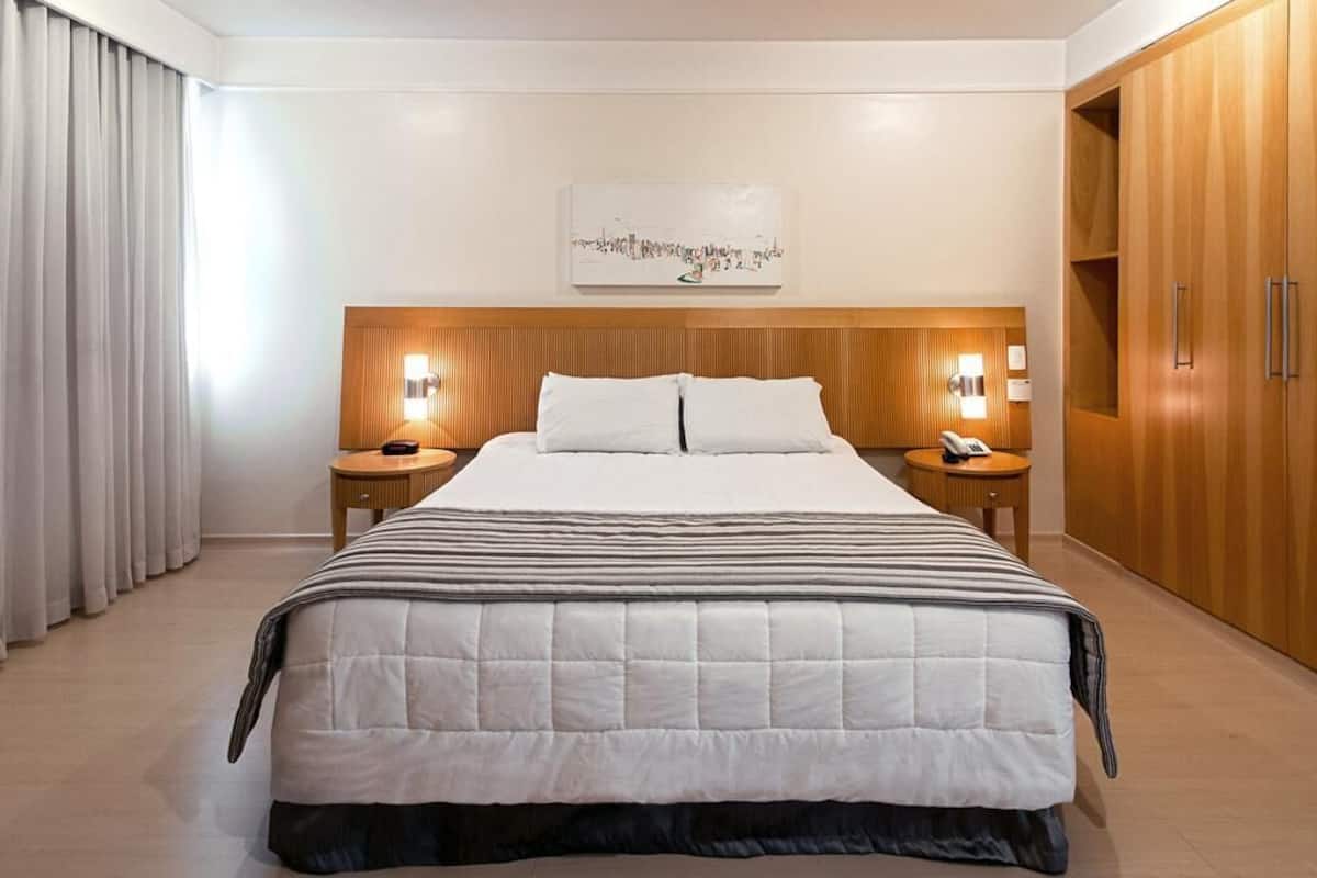 Ein Hotelzimmer mit einem großen Bett, einem Holzkopfteil, Nachttischlampen und einem Kleiderschrank.