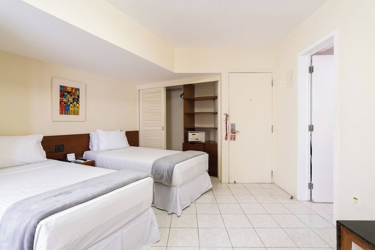 Habitación de hotel con dos camas, una mesita de noche, microondas, armario y puerta.