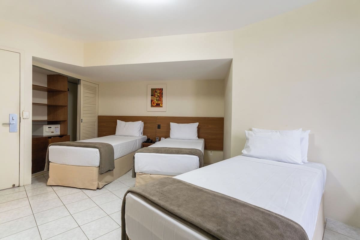 Habitación de hotel con dos camas individuales, cabecero de madera, mesita de noche con teléfono y una obra de arte colgada en la pared.