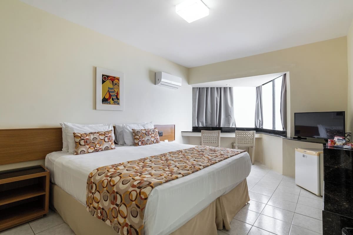Una habitación de hotel con cama, escritorio, televisor y ventana con cortinas.