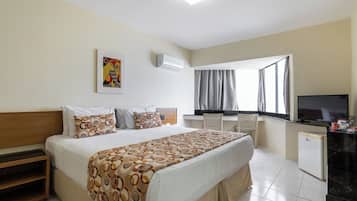A hotel room with a bed, a desk, a television, and a window with curtains.