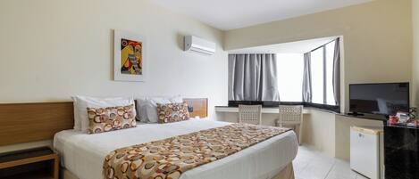 A hotel room with a bed, a desk, a television, and a window with curtains.