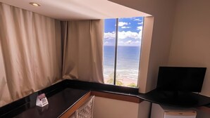 A small kitchenette with a counter, a chair, a television, and a window with a view of the sea. - Hotel Euro Suíte Recife By Nacional Inn (Recife)