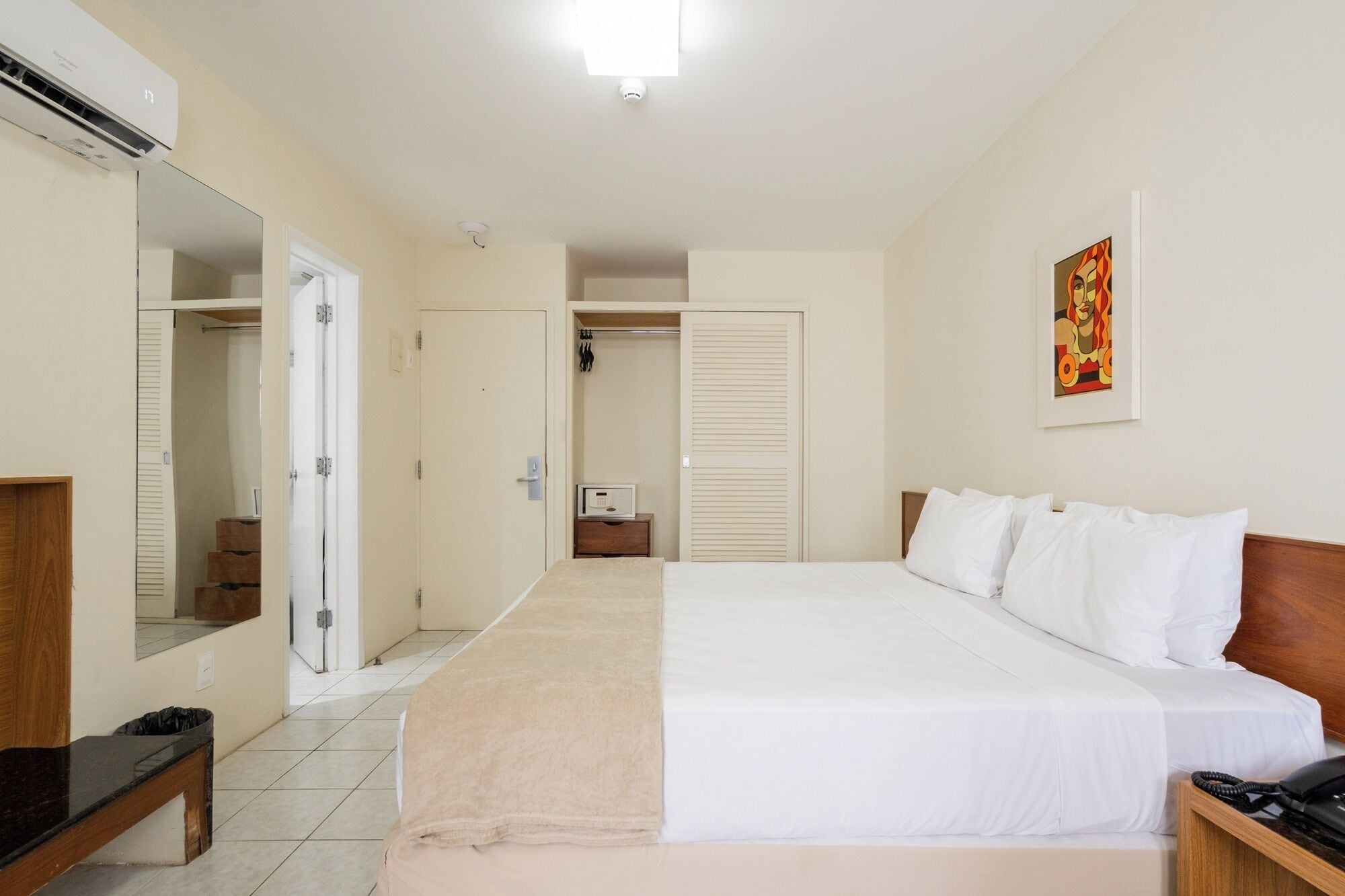 Una habitación de hotel con una cama grande, una mesita de noche, un espejo, un armario y un cuadro en la pared.