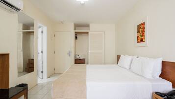Una habitación de hotel con una cama grande, una mesita de noche, un espejo, un armario y un cuadro en la pared.