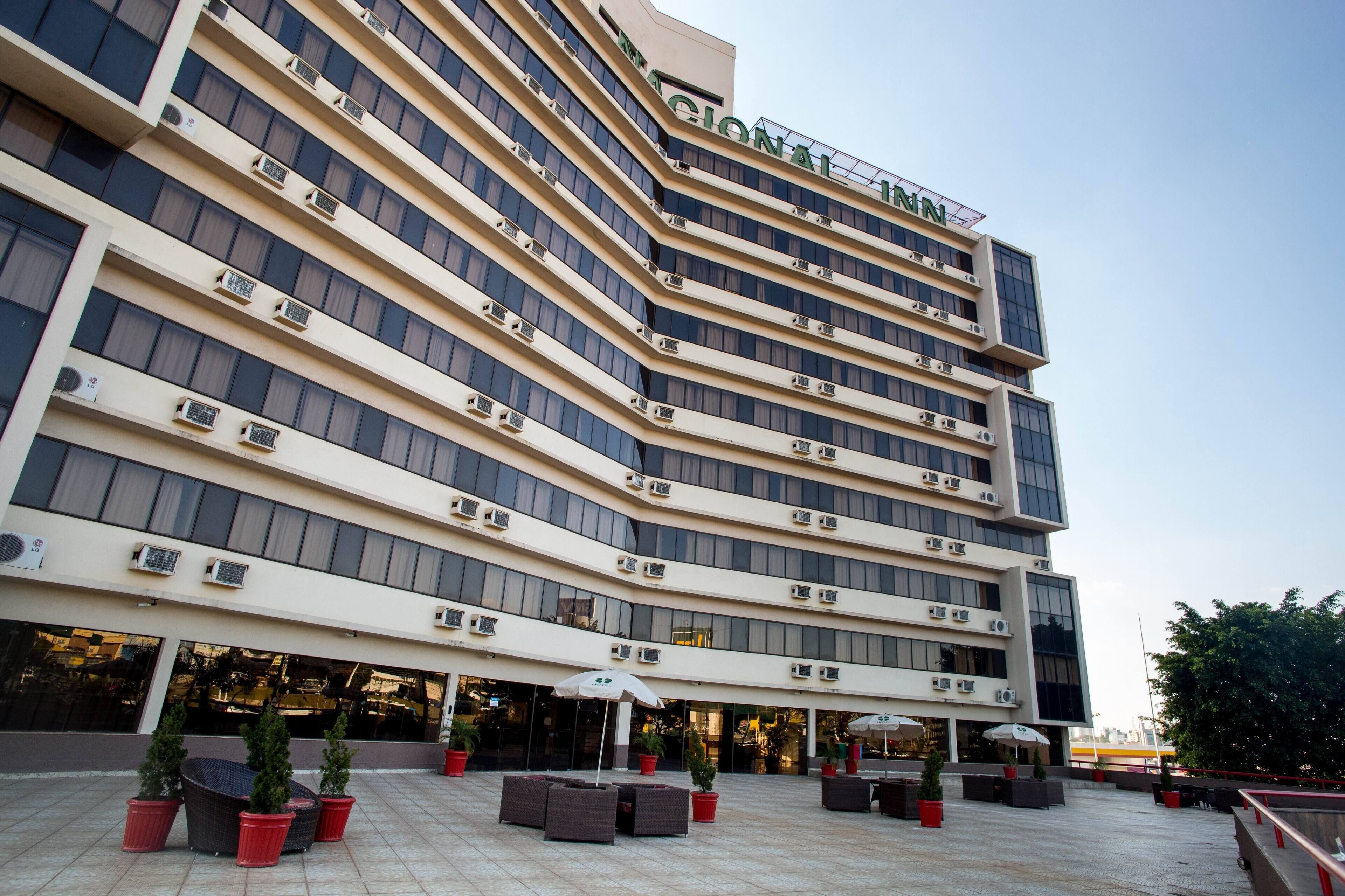 A multi-story hotel with a modern design, featuring a curved facade, large windows, and outdoor seating areas with umbrellas.