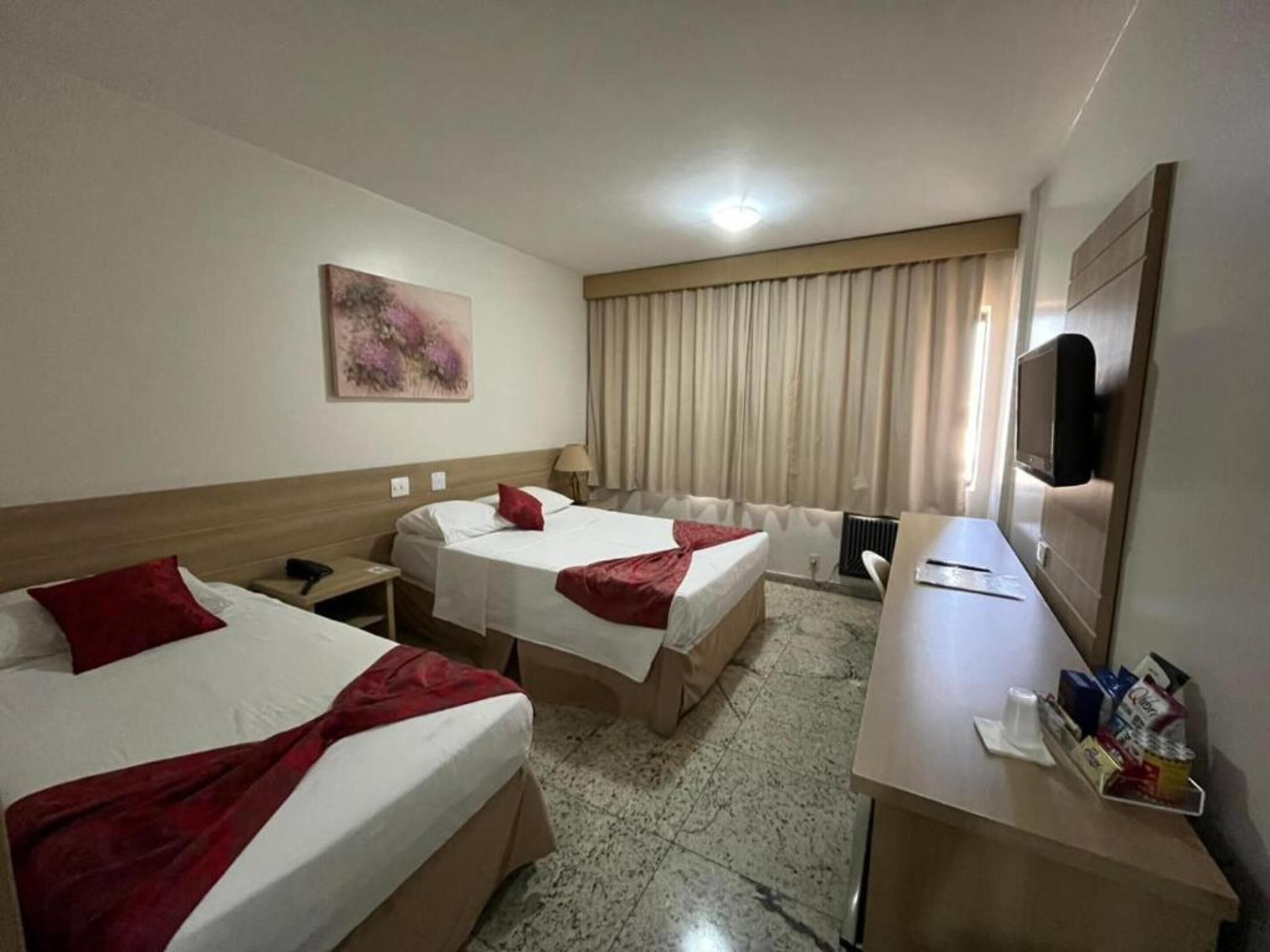 Una habitación de hotel con dos camas, un escritorio, un televisor y un cuadro en la pared.