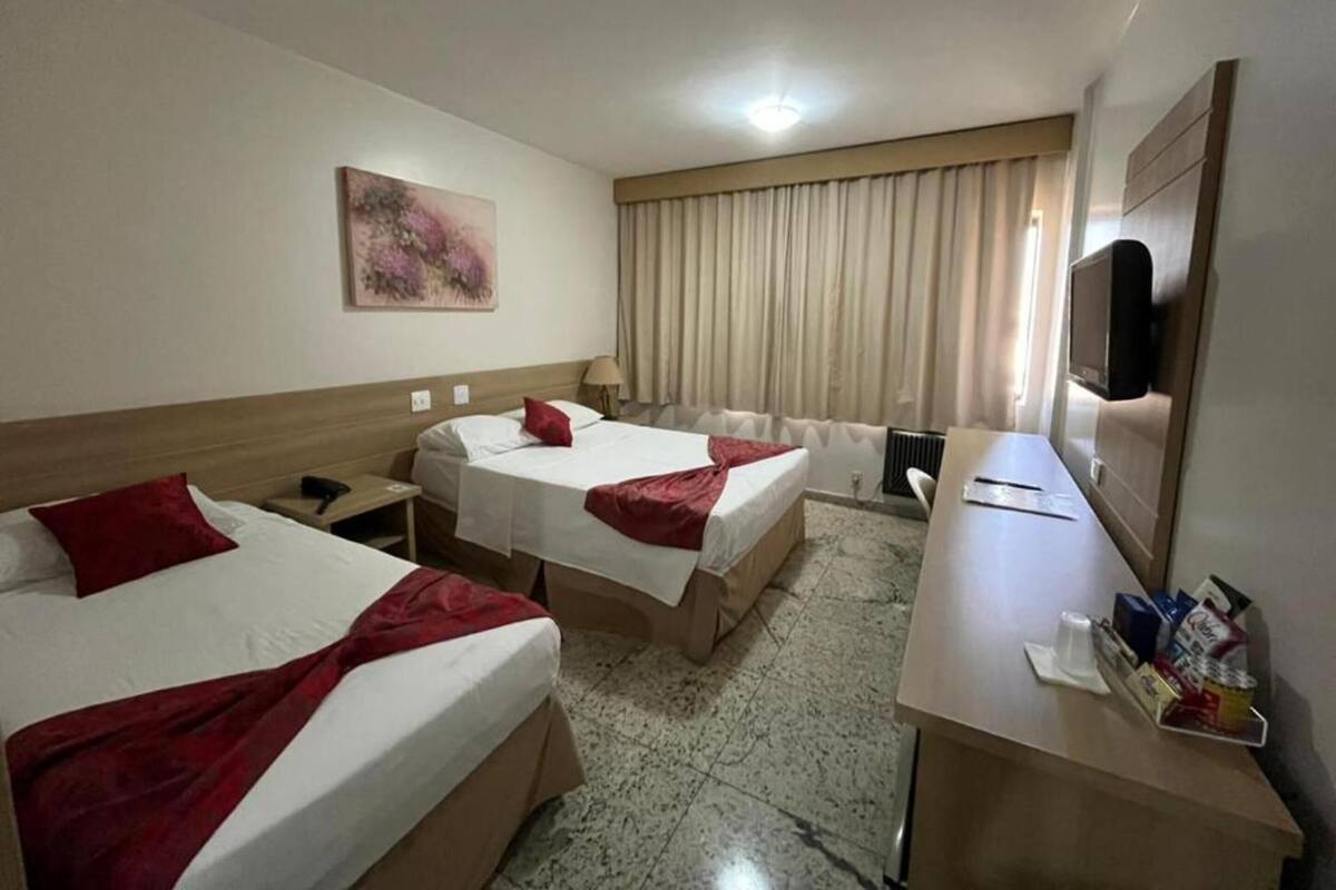 A hotel room with two beds, a desk, a television, and a painting on the wall.