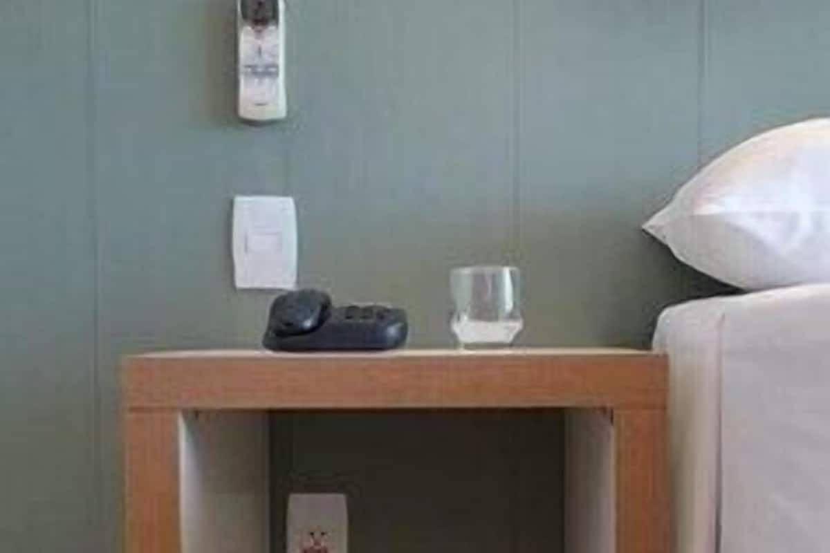 Ein Nachttisch aus Holz mit einer Ablage, einer Fernbedienung, einem Glas und einem kleinen Schild.