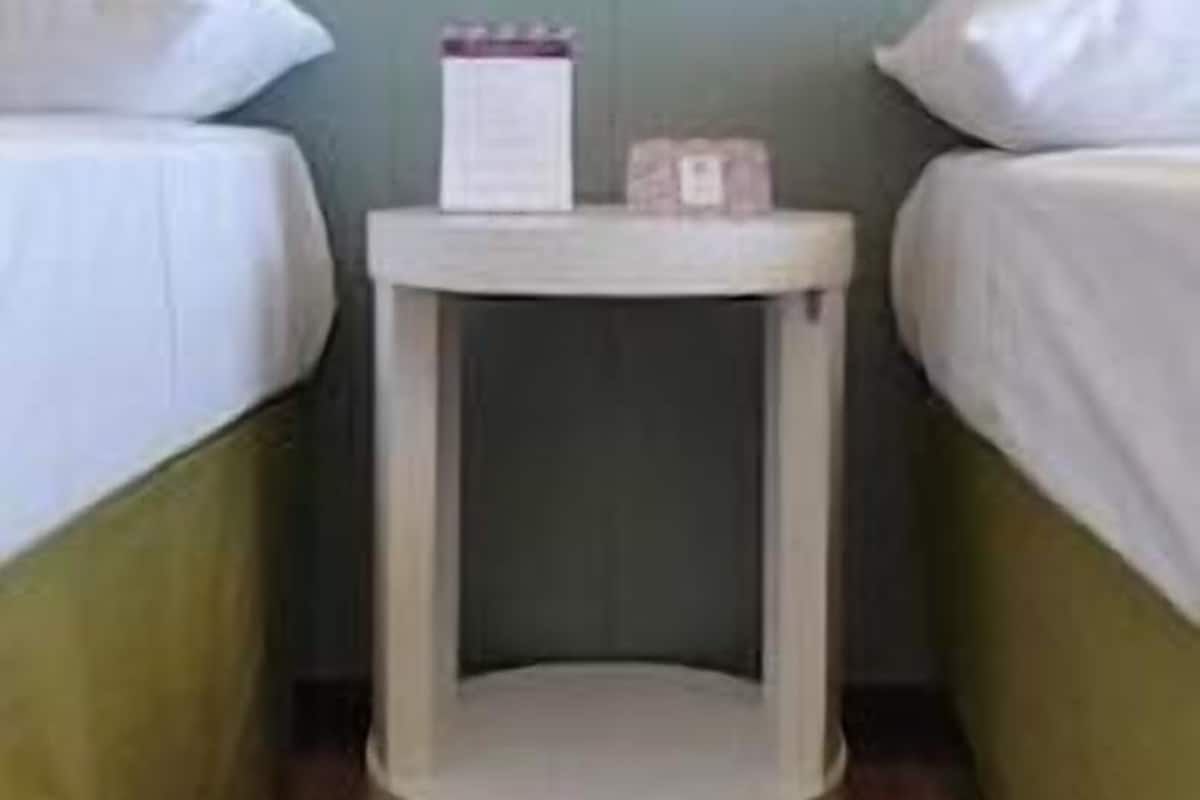 Ein Zimmer mit zwei Betten, einem kleinen Nachttisch und einem an der Wand befestigten Regal.