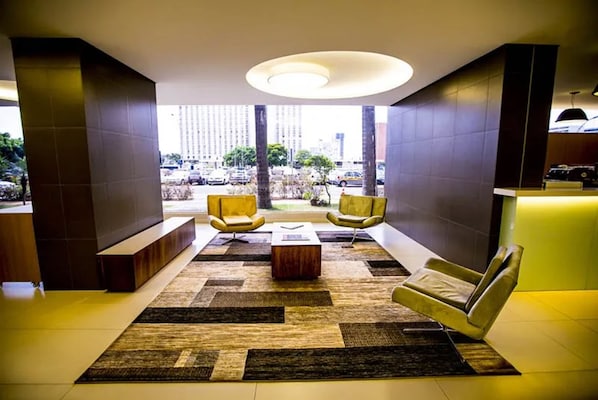 Un vestíbulo moderno con una mesa de centro, dos sillones amarillos y un ventanal con vistas a la ciudad.