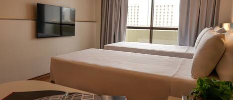 Habitación de hotel con cama, televisión en la pared, ventana con cortinas y planta sobre la mesita de noche.