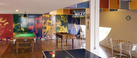 Una sala de billar con mesa de billar, mesa de fútbol de mesa y mesa de tenis de mesa.