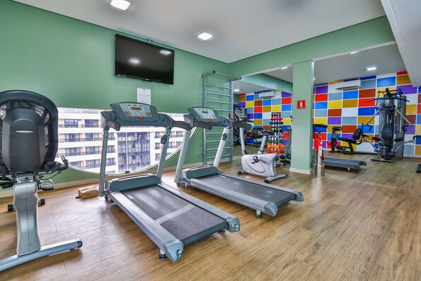 A gym with treadmills, a stationary bike, and a wall-mounted TV. - St. Paul Plaza (Brasília)