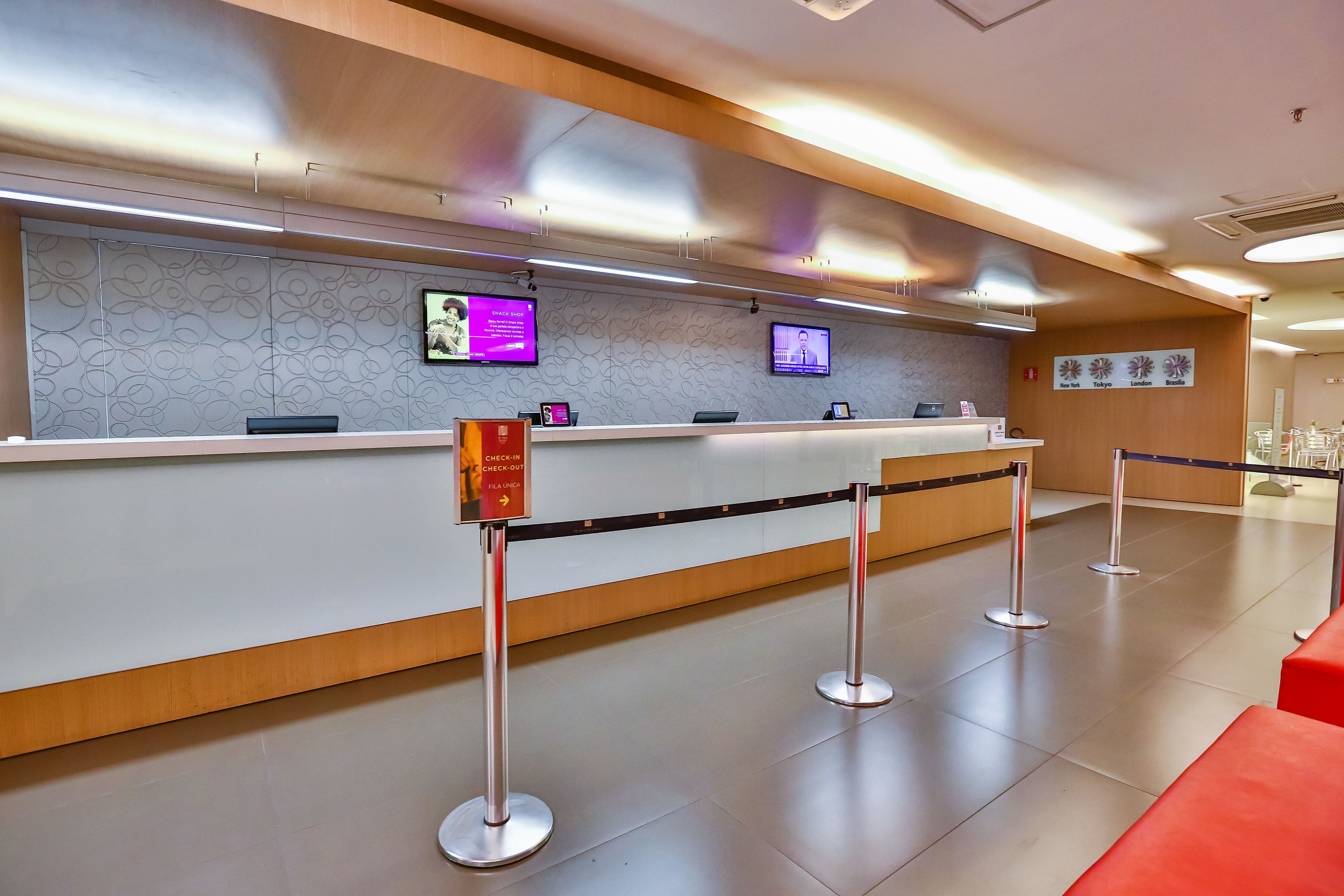 A reception area with a check-in counter, two monitors, a digital screen displaying information, and a sign indicating a check-in/out desk.