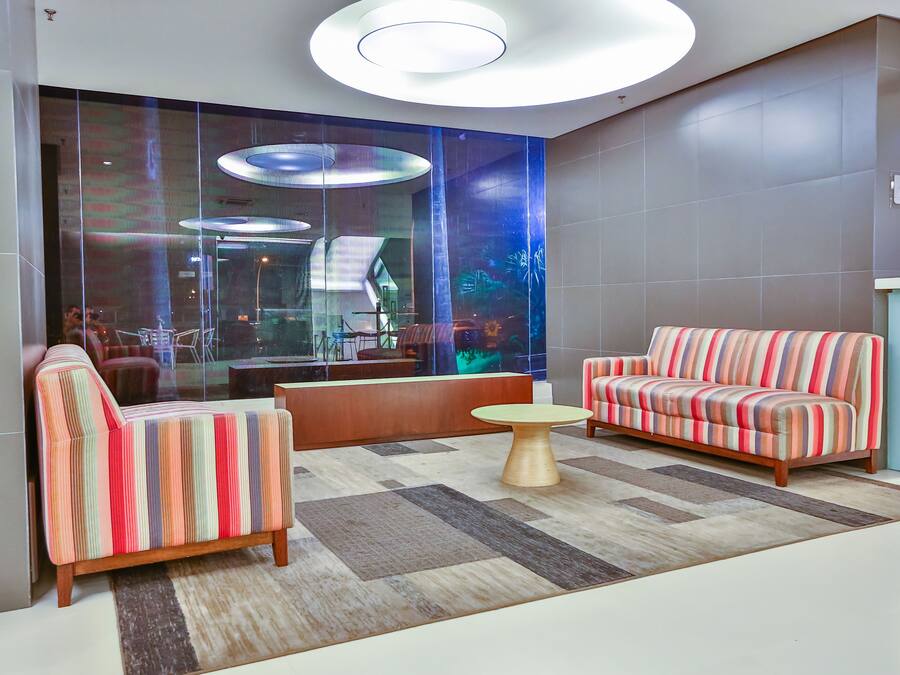 Un vestíbulo moderno con sofás a rayas, una mesa redonda de madera y un muro de cristal con una proyección.