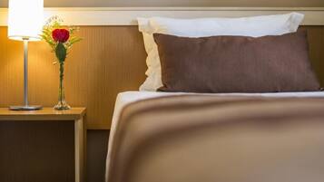 Una habitación de hotel con una cama bien hecha, una lámpara de noche y un jarrón con flores.