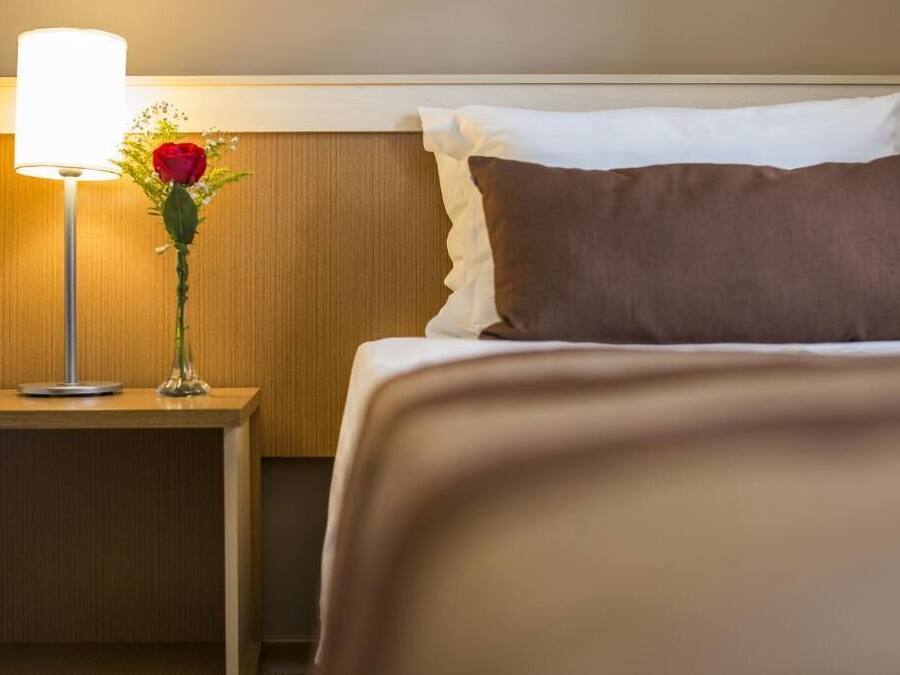 Una habitación de hotel con una cama bien hecha, una lámpara de noche y un jarrón con flores.