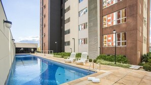 A swimming pool with lounge chairs and a tiled deck, surrounded by modern buildings. - Astron Hotel Bauru by Nobile (Bauru)