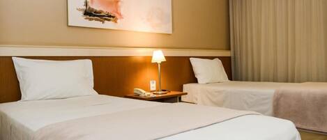 Una habitación de hotel con dos camas, una mesita de noche con lámpara y un cuadro en la pared.