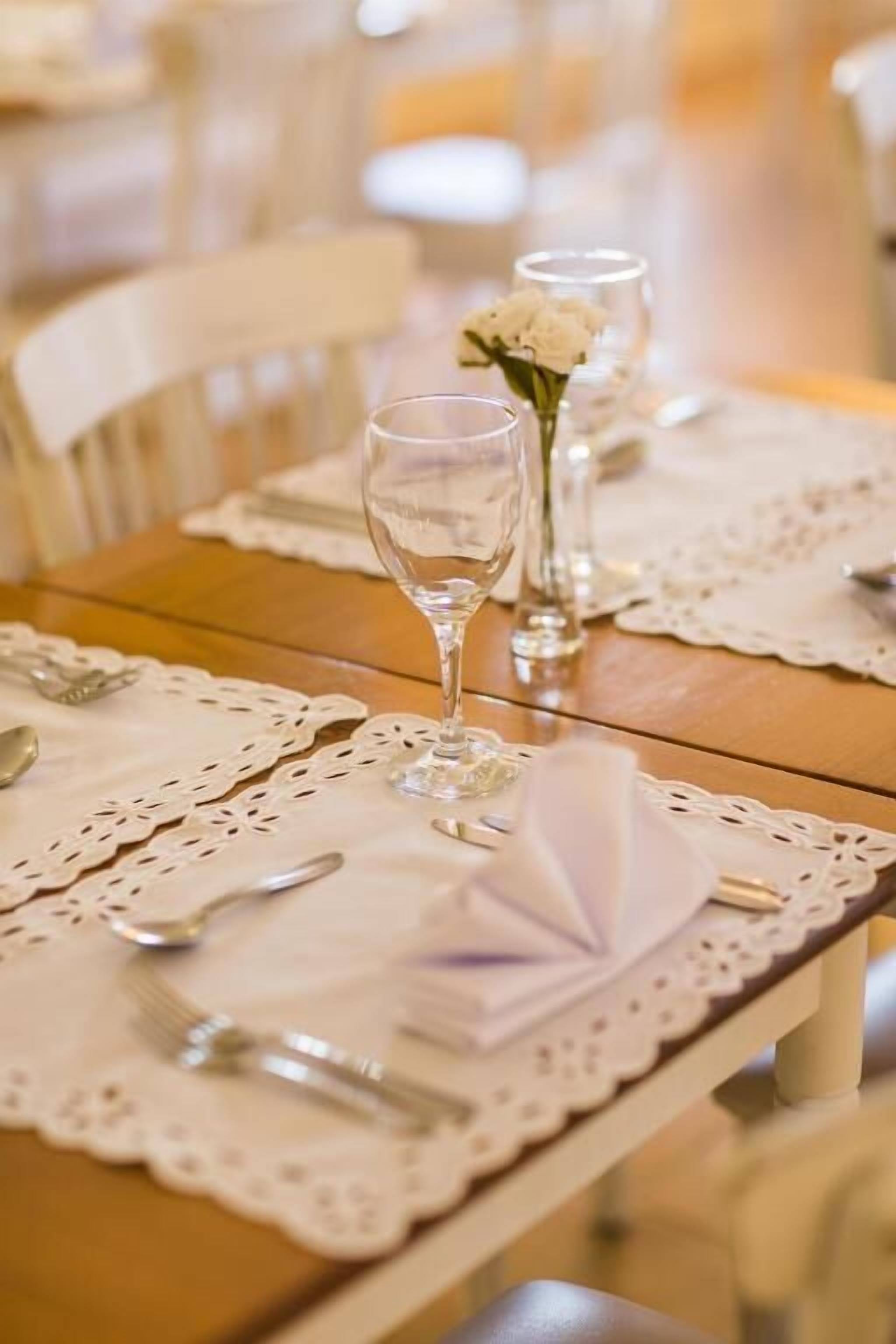 Mesa de jantar posta com toalhas de renda branca, talheres e copos de vidro.